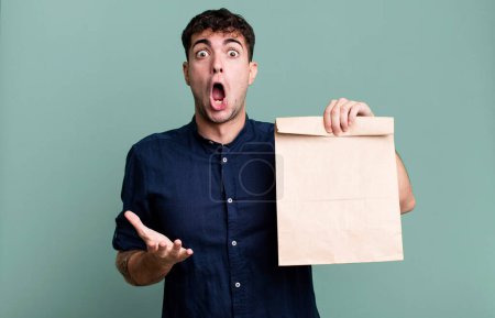 Téléchargez les photos : Homme adulte étonné, choqué et étonné avec une surprise incroyable avec un sac en papier à emporter petit déjeuner avec un sac en papier à emporter petit déjeuner - en image libre de droit
