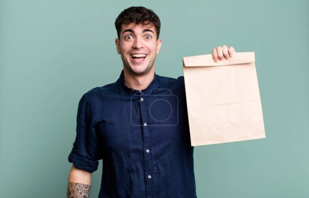 Téléchargez les photos : Homme adulte regardant heureux et agréablement surpris avec un sac à emporter petit déjeuner en papier avec un sac à emporter petit déjeuner en papier - en image libre de droit