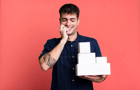 Téléchargez les photos : Homme adulte souriant avec une expression heureuse et confiante avec la main sur le menton avec des emballages de produits vierges - en image libre de droit