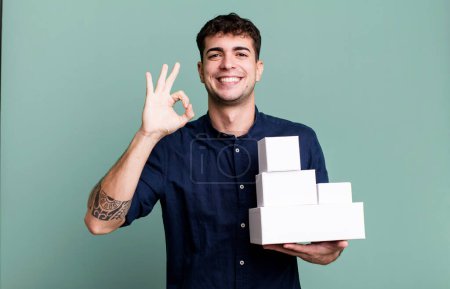 Téléchargez les photos : Homme adulte se sentant heureux, montrant l'approbation avec le geste correct avec des emballages de produits vierges - en image libre de droit