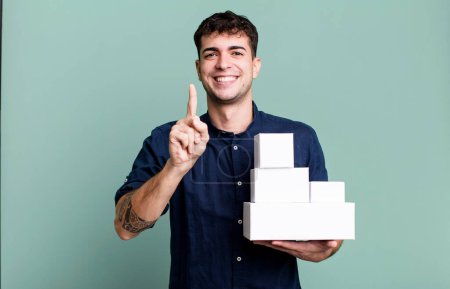Foto de Hombre adulto sonriendo orgullosamente y con confianza haciendo número uno con paquetes de productos en blanco - Imagen libre de derechos