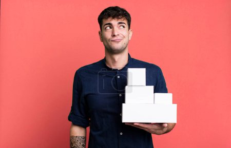 Foto de Hombre adulto encogiéndose de hombros, sintiéndose confundido e incierto con paquetes de productos en blanco - Imagen libre de derechos