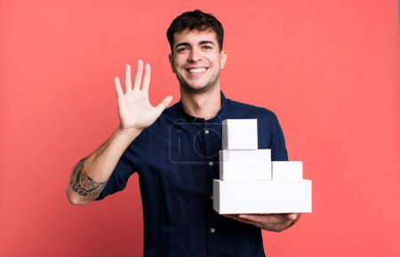 Téléchargez les photos : Homme adulte souriant heureux, main agitant, vous accueillant et vous saluant avec des emballages de produits vierges - en image libre de droit