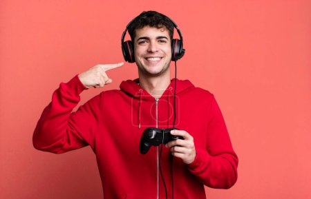 Foto de Hombre adulto sonriendo con confianza señalando a sí mismo amplia sonrisa con auriculares y un controlador. concepto de jugador - Imagen libre de derechos