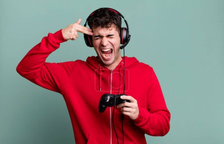 Foto de Hombre adulto que parece infeliz y estresado, gesto suicida haciendo señal de arma con auriculares y un controlador. concepto de jugador - Imagen libre de derechos
