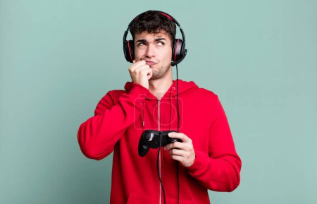 Foto de Hombre adulto pensando, sintiéndose dudoso y confundido con auriculares y un controlador. concepto de jugador - Imagen libre de derechos