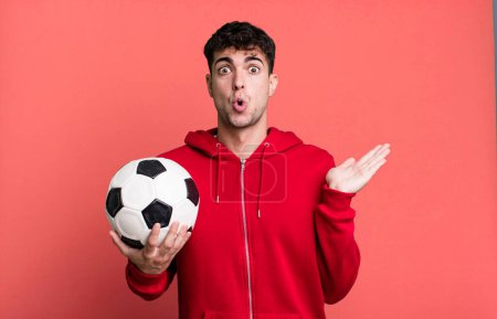 Foto de Hombre adulto mirando sorprendido y sorprendido, con la mandíbula caída sosteniendo un objeto. concepto de fútbol y deporte - Imagen libre de derechos