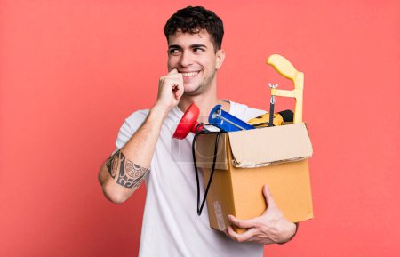 Foto de Hombre adulto sonriendo con una expresión feliz y segura con la mano en la barbilla con una caja de herramientas. concepto de ama de llaves - Imagen libre de derechos