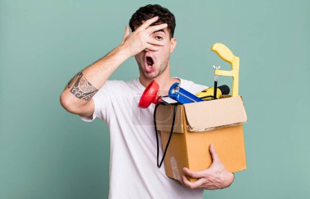 Photo for Adult man looking shocked, scared or terrified, covering face with hand with a toolbox. housekeeper concept - Royalty Free Image