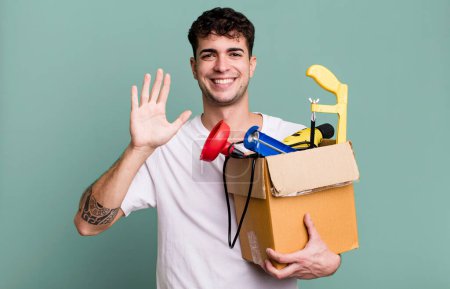 Foto de Hombre adulto sonriendo felizmente, saludando con la mano, dando la bienvenida y saludando con una caja de herramientas. concepto de ama de llaves - Imagen libre de derechos
