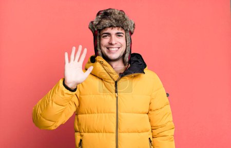 Foto de Hombre adulto sonriendo felizmente, saludando con la mano, dando la bienvenida y saludando vistiendo anorak. concepto de invierno y frío - Imagen libre de derechos