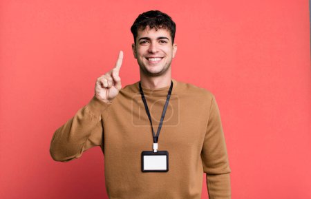 Foto de Hombre adulto sonriendo y buscando amigable, mostrando el número uno con una tarjeta de identidad de acceso - Imagen libre de derechos
