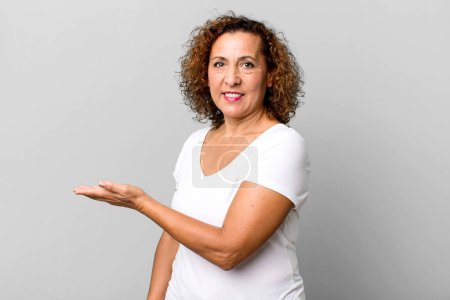 Photo for Middle age hispanic woman smiling cheerfully, feeling happy and showing a concept in copy space with palm of hand - Royalty Free Image