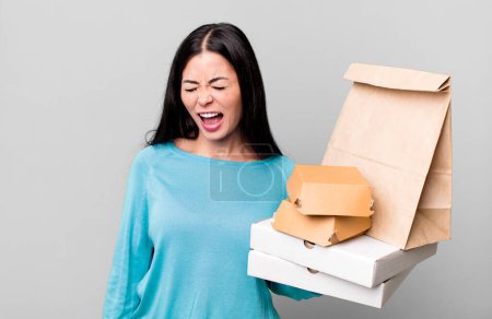 Foto de Mujer bonita hispana gritando agresivamente, pareciendo muy enojada. con paquetes de comida rápida para llevar - Imagen libre de derechos