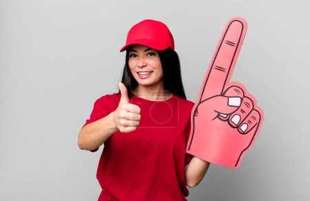 Téléchargez les photos : Hispanique jolie femme se sentant fière, souriant positivement avec les pouces levés. numéro un concept de ventilateur de main - en image libre de droit
