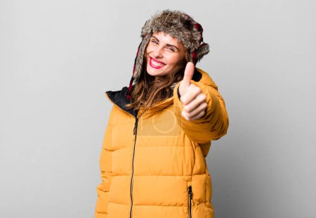 Téléchargez les photos : Hispanique jolie femme se sentant fière, souriant positivement avec les pouces levés. portant un anorak. concept froid et hiver - en image libre de droit