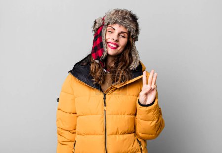 Foto de Mujer bonita hispana sonriendo y luciendo amigable, mostrando el número tres. usando un anorak. concepto frío e invierno - Imagen libre de derechos