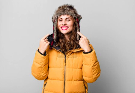 Foto de Hispanic pretty woman smiling confidently pointing to own broad smile. wearing an anorak. cold and winter concept - Imagen libre de derechos