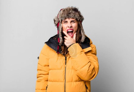 Photo for Hispanic pretty woman with mouth and eyes wide open and hand on chin. wearing an anorak. cold and winter concept - Royalty Free Image