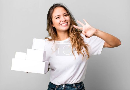 Téléchargez les photos : Hispanic pretty woman smiling and looking friendly, showing number three with white boxes packages - en image libre de droit