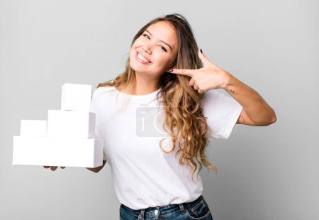 Foto de Mujer bonita hispana sonriendo con confianza apuntando a su propia sonrisa amplia con paquetes de cajas blancas - Imagen libre de derechos