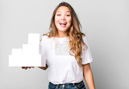 Photo for Hispanic pretty woman looking happy and pleasantly surprised with white boxes packages - Royalty Free Image