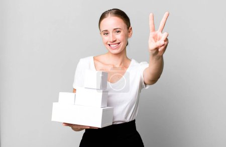 Téléchargez les photos : Caucasian pretty woman smiling and looking happy, gesturing victory or peace with white boxes packages - en image libre de droit