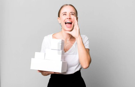 Foto de Caucasian pretty woman feeling happy,giving a big shout out with hands next to mouth with white boxes packages - Imagen libre de derechos