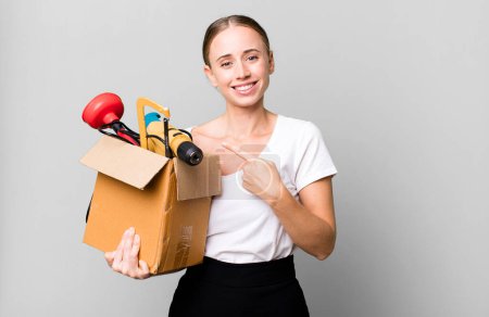 Foto de Caucasian pretty woman smiling cheerfully, feeling happy and pointing to the side with a tool box. repair home concept - Imagen libre de derechos