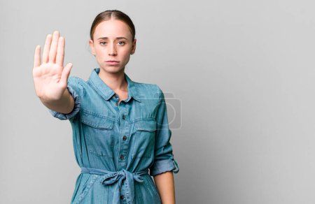 Foto de Caucasian pretty woman looking serious showing open palm making stop gesture - Imagen libre de derechos