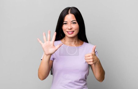 Foto de Mujer latina bonita sonriendo y buscando amigable, mostrando el número seis o sexto con la mano hacia adelante, cuenta atrás - Imagen libre de derechos