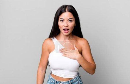 Foto de Pretty latin woman feeling shocked, astonished and surprised, with hand on chest and open mouth, saying who, me? - Imagen libre de derechos