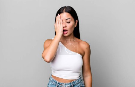 Photo for Pretty latin woman looking sleepy, bored and yawning, with a headache and one hand covering half the face - Royalty Free Image