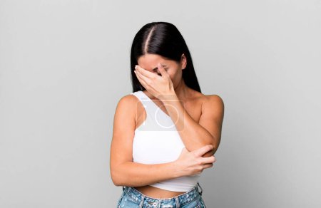Photo for Pretty latin woman looking stressed, ashamed or upset, with a headache, covering face with hand - Royalty Free Image