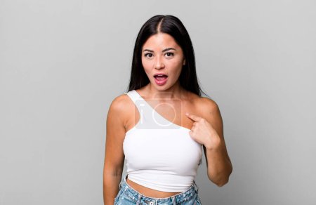 Photo for Pretty latin woman looking shocked and surprised with mouth wide open, pointing to self - Royalty Free Image