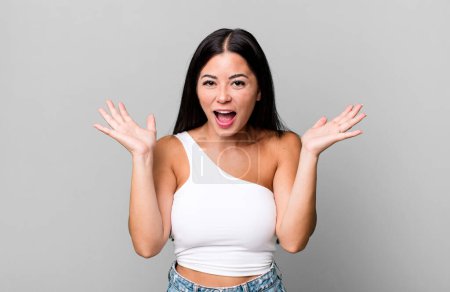 Foto de Pretty latin woman looking happy and excited, shocked with an unexpected surprise with both hands open next to face - Imagen libre de derechos