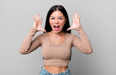 Foto de Pretty latin woman screaming with hands up in the air, feeling furious, frustrated, stressed and upset - Imagen libre de derechos