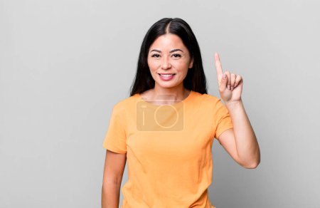 Téléchargez les photos : Jolie femme latine souriant joyeusement et joyeusement, pointant vers le haut avec une main pour copier l'espace - en image libre de droit