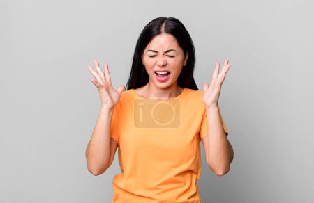 Photo for Pretty latin woman furiously screaming, feeling stressed and annoyed with hands up in the air saying why me - Royalty Free Image