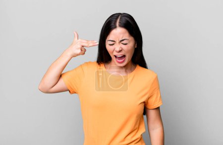 Téléchargez les photos : Pretty latin woman looking unhappy and stressed, suicide gesture making gun sign with hand, pointing to head - en image libre de droit
