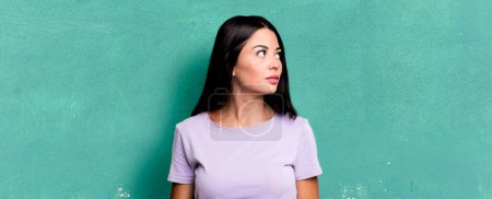 Foto de Pretty latin woman with a worried, confused, clueless expression, looking up to copy space, doubting - Imagen libre de derechos