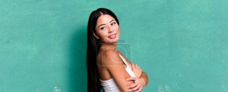 Foto de Pretty latin woman smiling gleefully, feeling happy, satisfied and relaxed, with crossed arms and looking to the side - Imagen libre de derechos