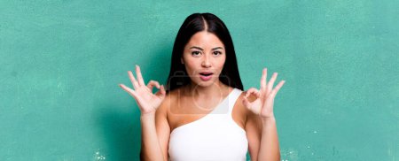 Photo for Pretty latin woman feeling shocked, amazed and surprised, showing approval making okay sign with both hands - Royalty Free Image