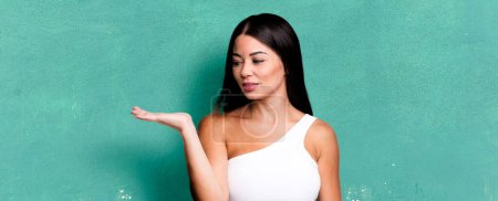 Photo for Pretty latin woman feeling happy and smiling casually, looking to an object or concept held on the hand on the side - Royalty Free Image