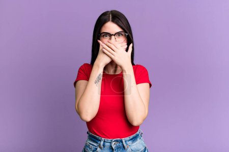 Photo for Young adult pretty woman covering mouth with hands with a shocked, surprised expression, keeping a secret or saying oops - Royalty Free Image
