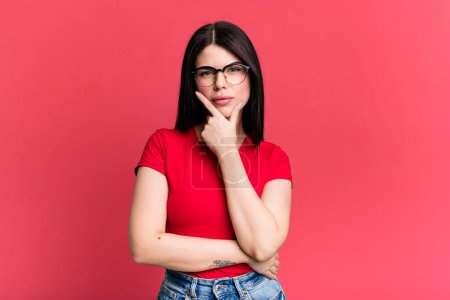 Photo for Young adult pretty woman looking serious, thoughtful and distrustful, with one arm crossed and hand on chin, weighting options - Royalty Free Image