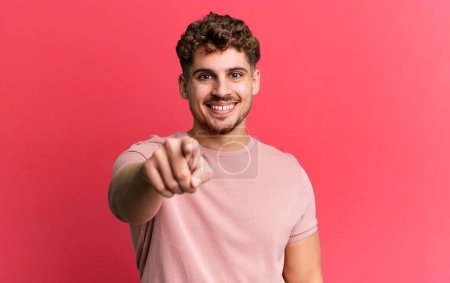 young adult caucasian man pointing at camera with a satisfied, confident, friendly smile, choosing you