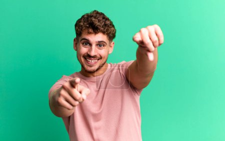 Téléchargez les photos : Young adult caucasian man feeling happy and confident, pointing to camera with both hands and laughing, choosing you - en image libre de droit