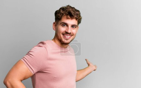 Téléchargez les photos : Young adult caucasian man feeling happy and cheerful, smiling and welcoming you, inviting you in with a friendly gesture - en image libre de droit