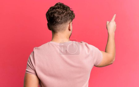 Foto de Young adult caucasian man standing and pointing to object on copy space, rear view - Imagen libre de derechos